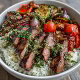 Fluffy rice topped with tender grilled steak, roasted zucchini and peppers, and bright green chimichurri in a bowl.