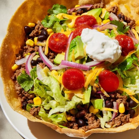 Crispy tortilla bowl overflowing with a flavorful taco salad featuring seasoned beef and fresh toppings.