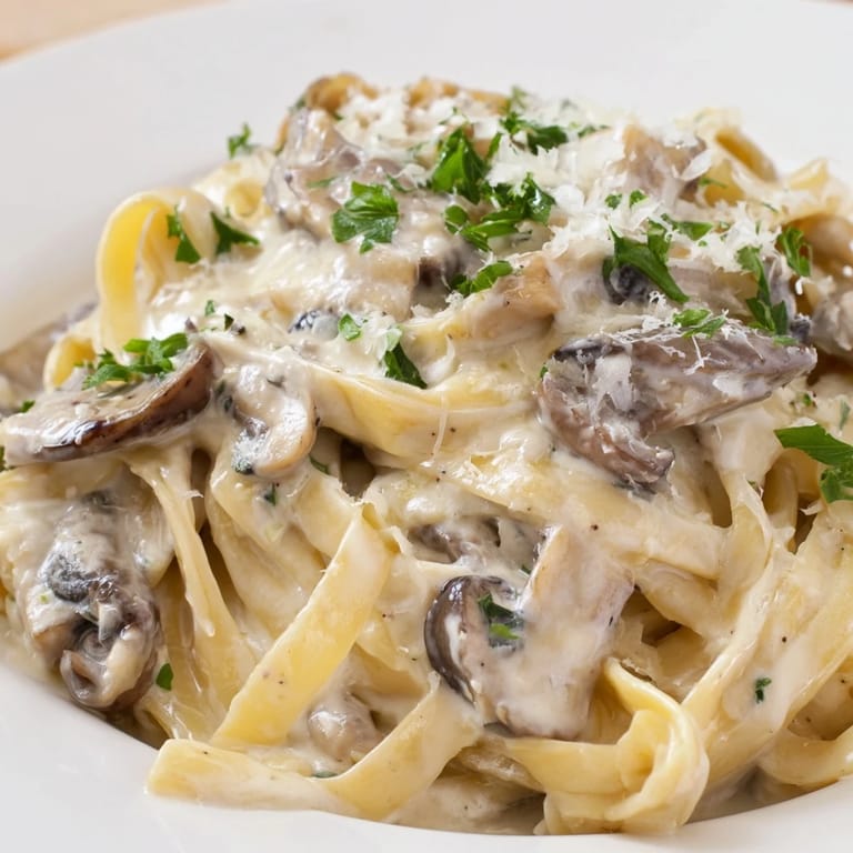 Creamy Mushroom Alfredo is served alongside a crisp green salad on a rustic wooden table.