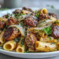 Steaming plate of Winter Pasta with Sausage and Fennel, savory crumbles and golden noodles garnished with fresh green fronds.