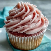 Moist, blush-pink Pink Velvet Cupcakes topped with fluffy vanilla buttercream and colorful sprinkles on a marble countertop.