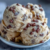 Scoops of Greek Yogurt Cookie Dough are studded with mini chocolate chips and served chilled in a small white bowl.