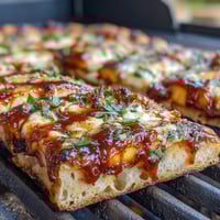 Grilled flatbread topped with juicy peaches, melted Brie, and smoky BBQ sauce, garnished with fresh basil.